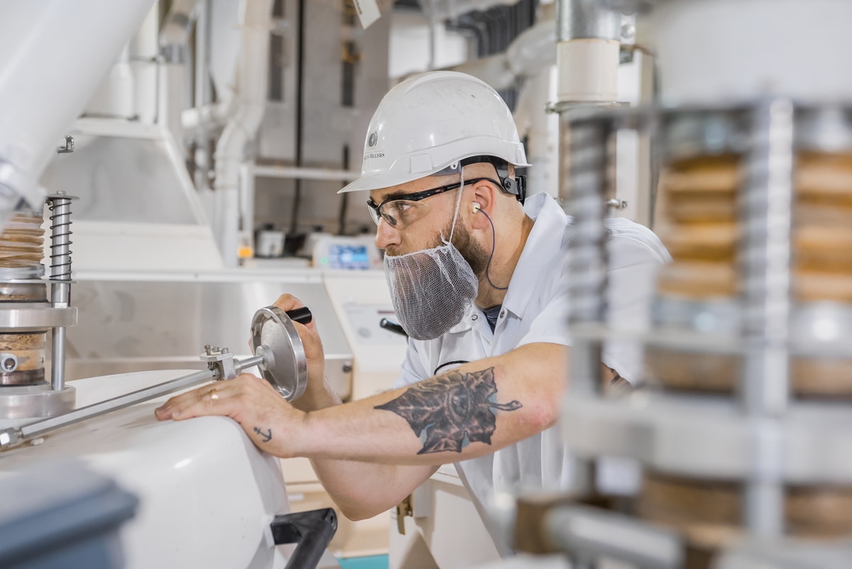 Man making adjustments on milling equipment wearing safety gear in the Grain Millers factory.